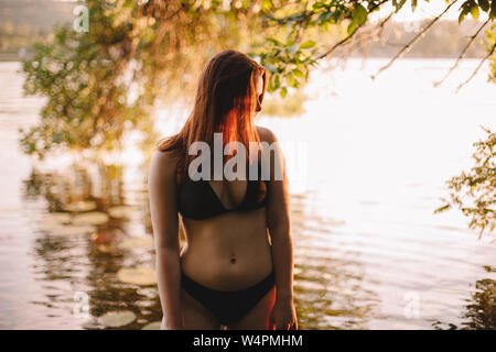 Woman in a bikini standing in lake under tree Banque D'Images