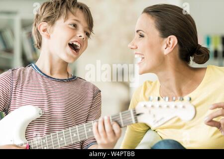 La mère et le fils de faire de la musique ensemble, tant le chant et son playing electric guitar, close-up, rire, Allemagne Banque D'Images