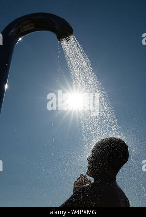 Bielefeld, Allemagne. 24 juillet, 2019. Un homme prend une douche dans la lumière arrière du soleil sous une douche dans une piscine extérieure. Credit : Friso Gentsch/dpa/Alamy Live News Banque D'Images