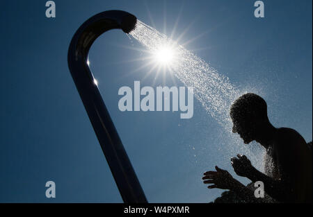 Bielefeld, Allemagne. 24 juillet, 2019. Un homme prend une douche dans la lumière arrière du soleil sous une douche dans une piscine extérieure. Credit : Friso Gentsch/dpa/Alamy Live News Banque D'Images