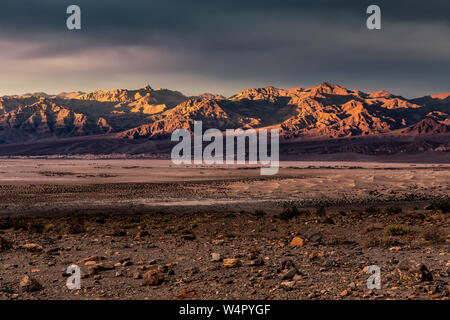 Le coucher du soleil illuminant les montagnes funéraire dans la vallée de la mort avec Mesquite Flat dunes de sable à l'avant-plan. Banque D'Images