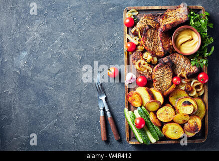 Schwenkbraten, juteux, fumé allemand grillé côtelettes de porc sont cuites sur un grill servi sur une planche à découper grossier avec des tranches de pommes de terre, oignon, Banque D'Images
