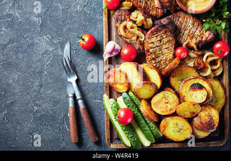 Schwenkbraten, juteux, fumé allemand grillé côtelettes de porc sont cuites sur un grill servi sur une planche à découper impoli avec pommes de terre rôties, oignons frits, Banque D'Images