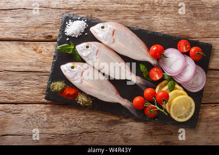 Dorado non cuits ou de la brème de mer Poisson aux épices, tomate, oignon et citron close up sur un conseil d'ardoise sur la table supérieure horizontale. vue de abov Banque D'Images