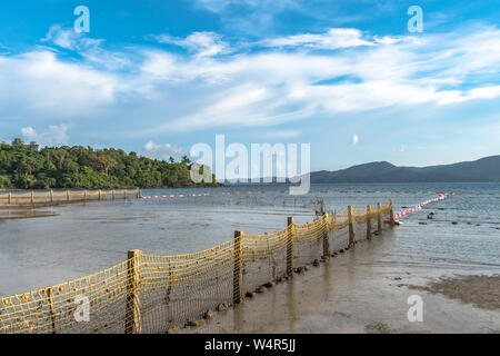 Paysage côtier de plage à marée basse, où pour les nageurs de clôtures de sécurité,la compensation a fait. Forêt de mangrove en arrière-plan avec ciel bleu et nuages Banque D'Images