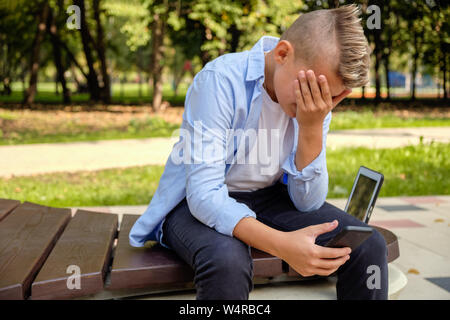 Problèmes d'enfants. moderne Jeune homme dans le parc avec le téléphone en colère. La dépression est un trouble mental dû à des réseaux sociaux. La vie en ligne Banque D'Images