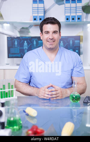 Portrait of male scientist in lab recherche portant son uniforme et souriant à la caméra. Tubes à essai avec green solutions. Banque D'Images