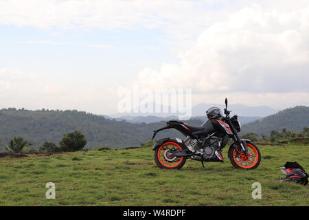 Une orange sports moto reposant sur une colline verte avec de belles montagnes en arrière-plan Banque D'Images