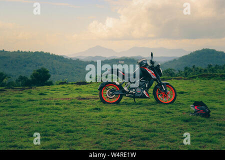 Une orange sports moto reposant sur une colline verte avec de belles montagnes en arrière-plan Banque D'Images