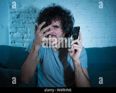 Portrait de jeune homme vie peur et choqué de faire peur, d'anxiété de gestes en regardant la télévision holding remote control. Dans une horreur Banque D'Images