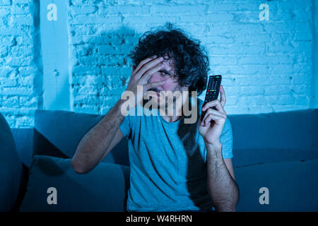 Portrait de jeune homme vie peur et choqué de faire peur, d'anxiété de gestes en regardant la télévision holding remote control. Dans une horreur Banque D'Images