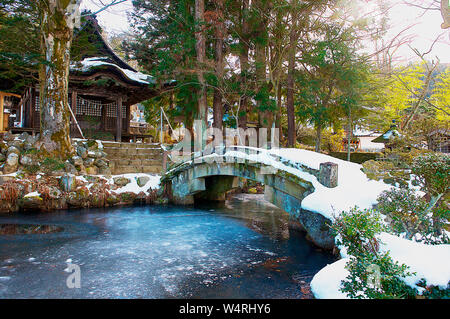 Passerelle en pierre recouvert de neige sur la rivière menant à une petite maison de bois, Hida-Takayama, Takayama, préfecture de Gifu, Japon Banque D'Images