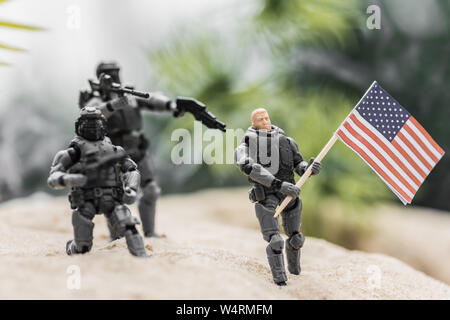 Focus sélectif de petits soldats visant à feu à toy man avec le drapeau américain sur la colline de sable Banque D'Images