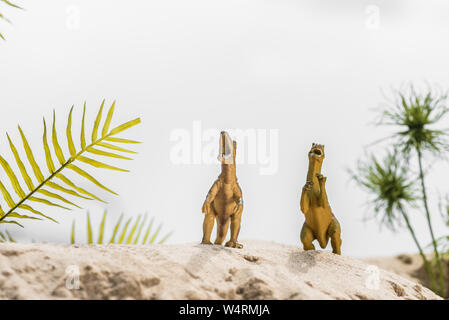Focus sélectif de dinosaures jouets roaring sur dune de sable avec des feuilles tropicales Banque D'Images