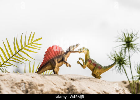 Focus sélectif de dinosaures jouets roaring sur dune de sable avec des feuilles exotiques Banque D'Images