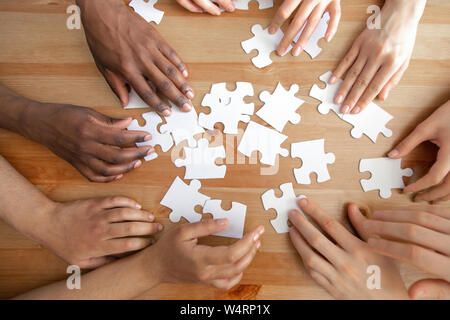 Close up haut au-dessus de la diversité des mains de l'assemblage des puzzles. Banque D'Images