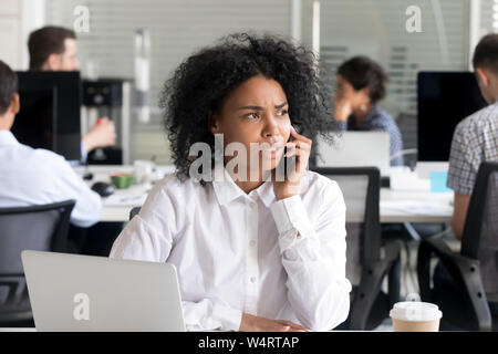 Malheureux African American Woman talking on téléphone au travail Banque D'Images