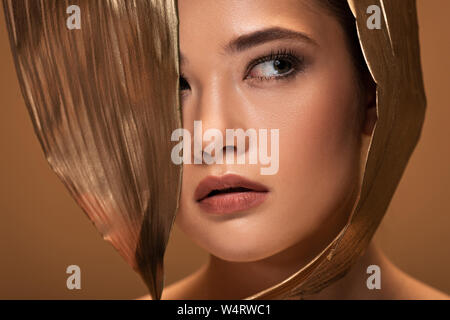 Portrait de belle jeune femme avec des feuilles d'or à l'écart isolé sur beige Banque D'Images