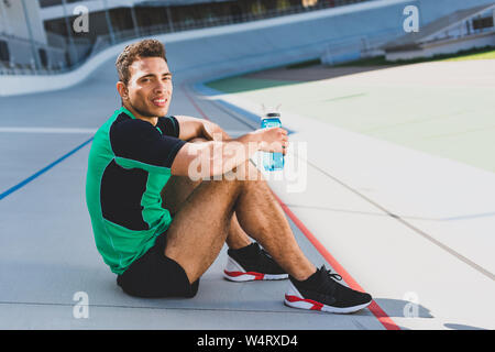 Mixed Race sportsman assis sur une piste de course à stade, à la caméra et à la tenue d'eau l Banque D'Images