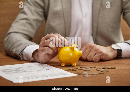 Portrait of businessman in suit la mise en pièce de tirelire en bois jaune à table Banque D'Images