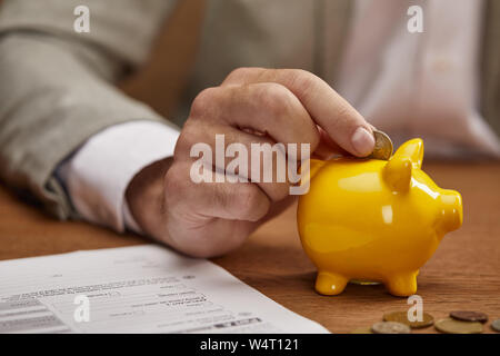 Vue rapprochée de businessman putting coins in piggy bank jaune à table en bois Banque D'Images