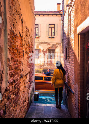 Venise, Italie, 17/11-18. Femme debout sur le bord d'un canal à la fin d'une ruelle. Un vieux classique, bateau, c'est passant. Banque D'Images