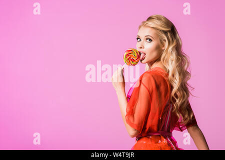 Beautiful Girl licking lollipop isolé sur rose, le concept de poupée Banque D'Images