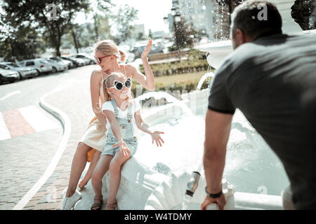 Best family. Joyeuse petite fille jouant avec ses parents près de belle fontaine blanche dans la ville. Banque D'Images