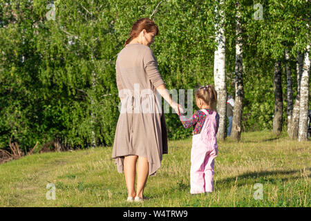 Dos de femme d'âge moyen et l'enfant se tenant par la main dans le parc avec des arbres d'été Banque D'Images