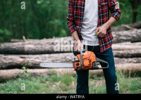 Vue partielle de bûcheron en chemise à carreaux holding chainsaw en forêt Banque D'Images