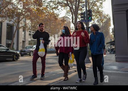 Un groupe d'amis génération du millénaire est titulaire d'emporter des sacs et marche le long de l'avenue University, à la Silicon Valley, à Palo Alto, en Californie, avec une femme portant un masque chirurgical pour protéger contre une traînée de fumée de l'incendie du camp 2018, le 17 novembre 2018. () Banque D'Images