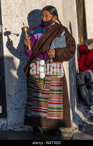 La Chine, Tibet, Lhasa, un Tibétain Khamba femme du Kham, région est du Tibet en pèlerinage à la Temple de Jokhang, elle porte une lourde traditionnelle doublée de mouton ou chupa chuba manteau et gangdian ou pangden tablier et de tourner son moulin à prières. Banque D'Images