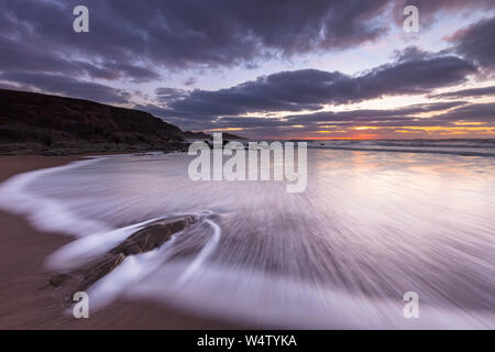 Débit d'ondes sur le sable et rochers au coucher du soleil à Welcombe Bouche Beach dans le Nord du Devon, Royaume-Uni. Banque D'Images