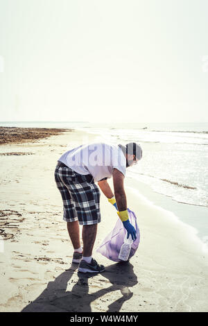 L'homme la collecte de matières plastiques qui polluent la mer dans un sac en plastique, des gens qui aident à conserver la nature propre et ramasser les déchets de plage, volunteer campai Banque D'Images