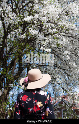 Femme debout à côté de l'arbre blanc en fleurs le jour ensoleillé Banque D'Images