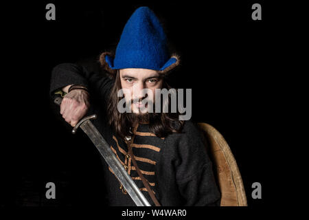 Guerrier barbu slaves dans un costume de l'ère viking prend l'épée de son fourreau, une allégorie de la force, protection, courage. Close up Banque D'Images