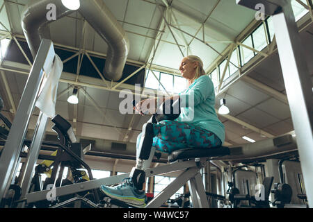 Mobilité active senior woman using mobile phone tout en exerçant in fitness studio Banque D'Images