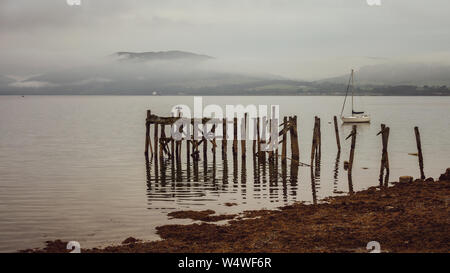 Le vieux, ruiné jetée en bois avec des montagnes derrière sur un jour brumeux - Port Bannatyne, île de Bute, Ecosse Banque D'Images