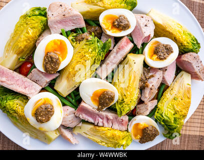 Version de salade niçoise sur plaque blanche. Oeufs durs et d'olive, vinaigrette laitue gem bébé, des pommes de terre et les tranches de steak de thon Banque D'Images