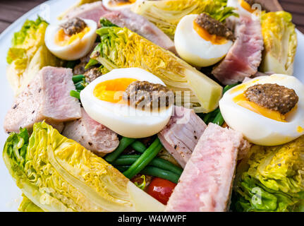 Version de salade niçoise sur plaque blanche. Oeufs durs et d'olive, vinaigrette laitue gem bébé, des pommes de terre et les tranches de steak de thon Banque D'Images