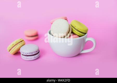 Image créative de sweet Biscuits macaron français colorés dans un mug blanc sur fond rose. Banque D'Images