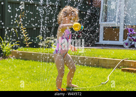 Un jeune enfant heureux qui garde au frais en jouant sous un arroseur d'eau de jardin, pendant la vague de chaleur estivale de 2019. Angleterre, Royaume-Uni apprendre par le jeu Banque D'Images