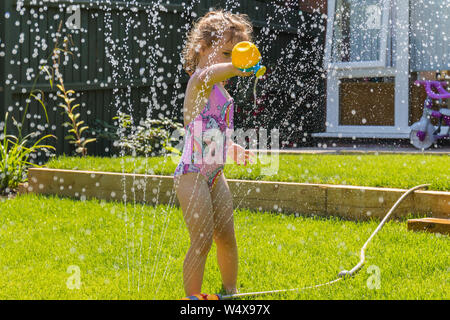 Un jeune enfant heureux qui garde au frais en jouant sous un arroseur d'eau de jardin, pendant la vague de chaleur estivale de 2019. Angleterre, Royaume-Uni apprendre par le jeu Banque D'Images