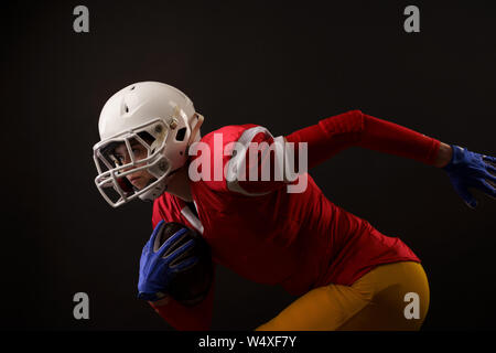 Photo de l'exécution de la sportive avec ballon de rugby, dans le casque blanc sur fond noir vide Banque D'Images