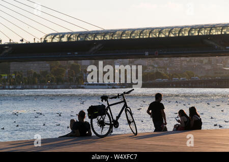 Istanbul, Turquie - le 19 juillet 2019 : un motard, sa moto un homme et deux jeunes femmes sont à la côte de la Corne d'or sur le parquet dans l'heure du coucher du soleil. Banque D'Images
