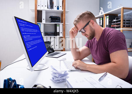 L'homme inquiet à l'ordinateur avec écran d'échec du système sur le lieu de travail Banque D'Images