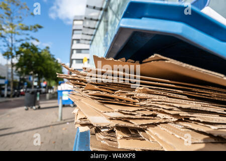 Utiliser des boîtes en carton aplati en attente d'être recueillie dans un récipient en plastique bleu pour la séparation et le recyclage des déchets de papier. Banque D'Images