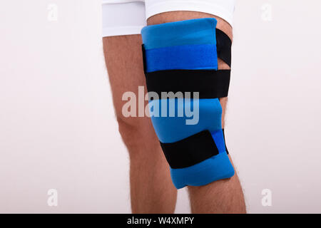 Close-up of a Man With Blue Ice Pack genou contre fond blanc Banque D'Images