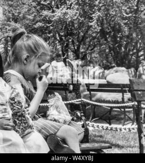 Portrait d'une jeune fille assise sur un banc de parc en plein air et d'alimentation électrique d'un sac de maïs, Detroit, Michigan, 1960. () Banque D'Images