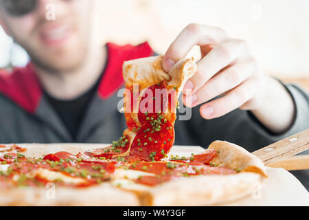 Young attractive smiling man eating pizza au café de la rue. Locations de. Fin de semaine. Repas de triche. Jour de triche. Régime alimentaire. Finition de l'alimentation. Banque D'Images